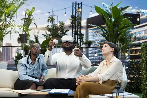 Businessman using VR headset next to coworkers on rooftop lounge Stock Photos