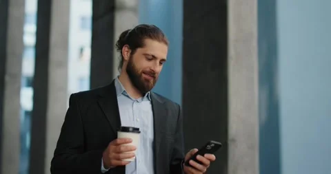 Businessman walking outside office while using smartphone, holding coffee. Stock Footage 246753814