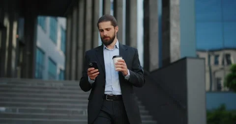 Businessman walking outside office while using smartphone, holding coffee. Stock Footage 246753930