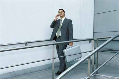 Businessman walking on sidewalk using cell phone, carrying briefcase Stock Photos