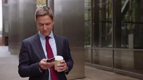 Businessman walking to work using smart phone with takeaway coffee Stock Footage 64981777