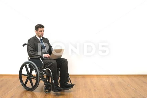 The businessman in a wheelchair sitting with a laptop on a white wall backgro Stock Photos