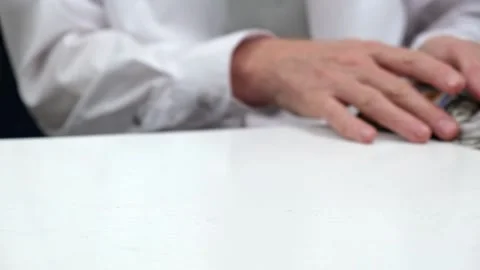 Businessman in a white shirt scoops stack of hundred-dollar bills from the table Stock Footage 183438735