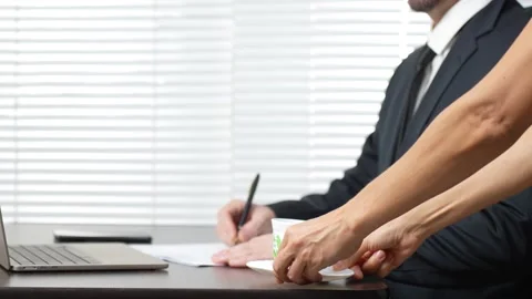 Businessman working at desk with document while secretary giving him coffee Stock Footage 291026996