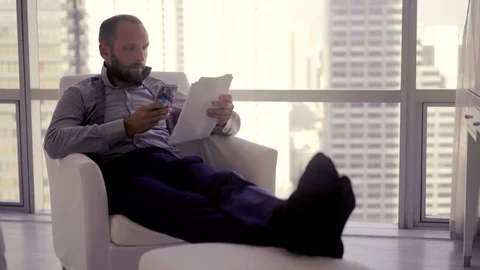 Businessman working with documents and smartphone sitting on armchair at home, 4 Stock Footage 83630747