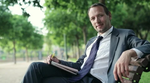 Businessman working with documents and smiling to camera in park, dolly shot HD Stock Footage 11149998