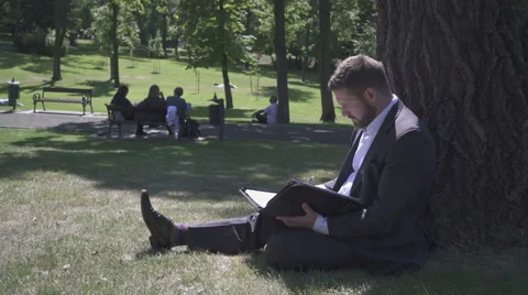 Businessman is working with documents, sitting under tree in park. 库存影片 52789237