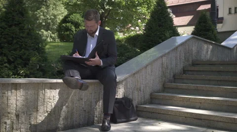 Businessman is working with documents, sitting on wall. Pan shot. 库存影片 52772827