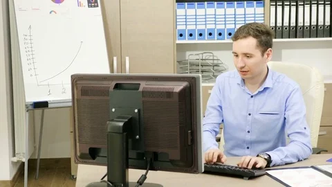 Businessman is working in his office at the computer next to folders filled with Stock Footage 83793464