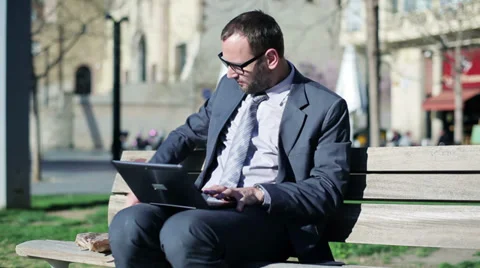 Businessman working on laptop and eating baguette on street bench. Stock Footage