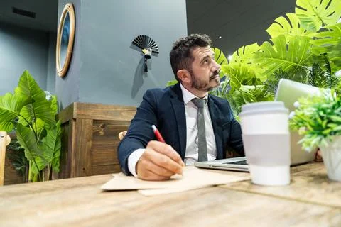 Businessman working with laptop and notes in modern office with plants Stock Photos