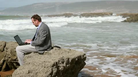 Businessman working on laptop computer on the rocks by the sea 스톡 동영상 10770118