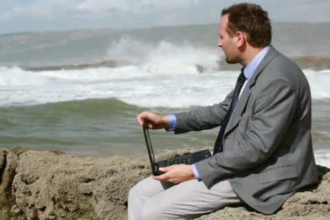 Businessman working on laptop computer on the rocks by the sea Stockbeeldmateriaal 10793342