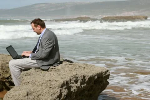 Businessman working on laptop computer on the rocks by the sea 스톡 동영상 10793345
