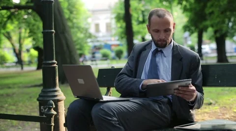 Businessman working on tablet computer and laptop in the city park HD Stock Footage 11134591