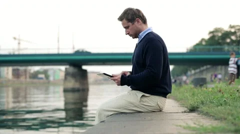 Businessman working on tablet computer by river in city, dolly shot HD Stock Footage 11874541