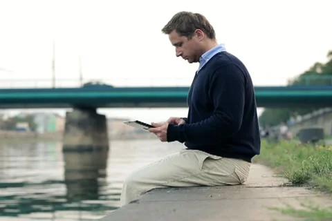Businessman working on tablet computer by river in city, dolly shot NTSC 스톡 동영상 11874543