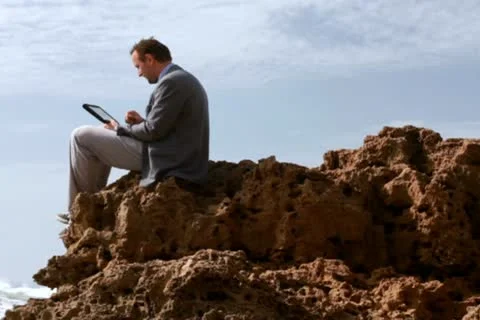 Businessman working on tablet computer on the rocks by the sea 스톡 동영상 10793351