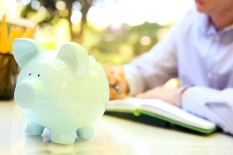 Businessman  writing in the notebook. A pig box behind Stock Photos