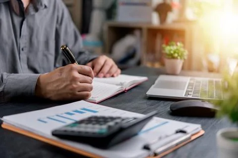 Businessman writing notes while working on financial reports at an office d.. Stock Photos