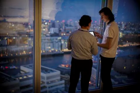 Businessmen with digital tablet working late at highrise office window Stock Photos
