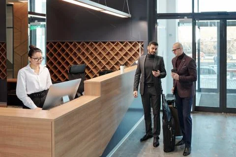 Businessmen discussing data in smartphone while receptionist using computer 写真素材