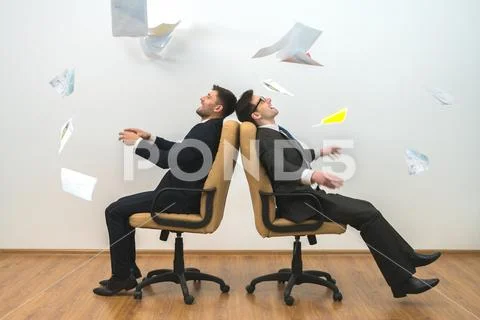The businessmen sit on chairs and throwing papers on the white wall backgroun Stock Photos