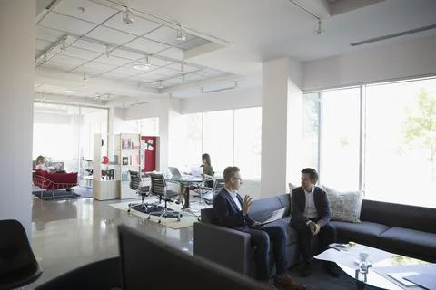 Businessmen talking on sofa in open plan office Fotos de archivo
