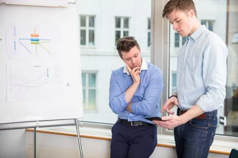 Businessmen Using Tablet Computer While Leaning On Window Sill Stock Photos