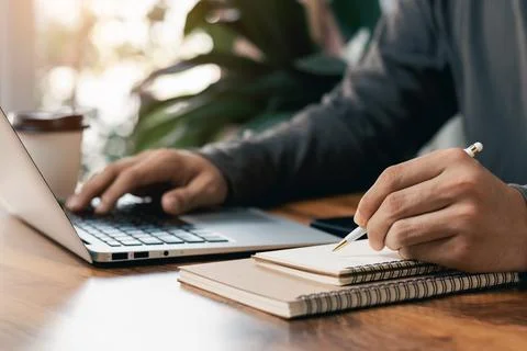 Businessmen work on computers and write on notepad with a pen to Calculate th Stock Photos