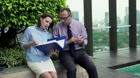 Businesspeople comparing data on documents and smartphone on terrace HD Stock Footage 51436663