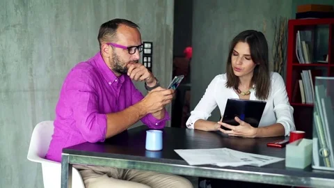 Businesspeople comparing data on tablet and smartphone sitting in the office Stock Footage 77035563