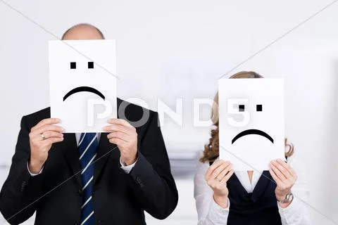 Businesspeople holding sad smileys on placard in front of faces Stock Photos