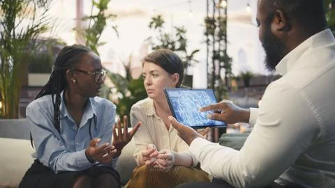Businesspeople using AI assistant on tablet to analyze data on rooftop lounge Stock Photos