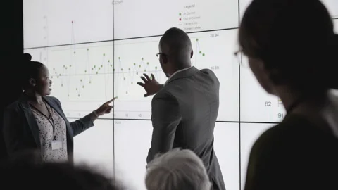 Businesspeople watching a multiscreen presentation by two African coworkers Stock Footage 138083285
