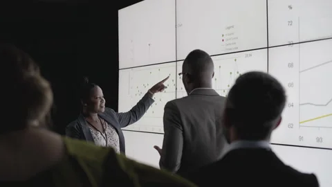 Businesspeople watching a multiscreen presentation by two African colleagues Stock Footage 138140342