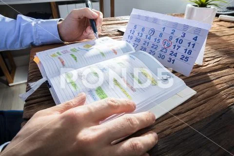 Businessperson's Hand Checking Schedule In Diary Stock Photos