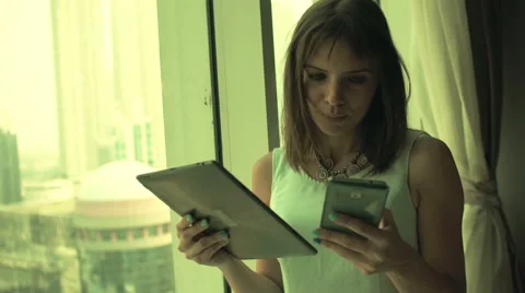 Businesswoman comparing data on tablet computer and smartphone by window Stock Footage 57378682
