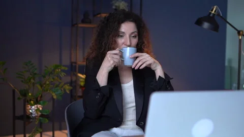 Businesswoman drinks tea while using a laptop. Attractive woman working late at Stock Footage 155484633
