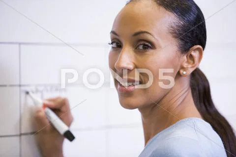 Businesswoman indoors writing on erasable board smiling Stock Photos