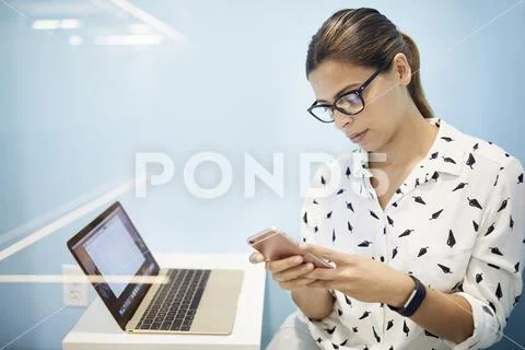 Businesswoman with laptop using smart phone in cubicle at office Stock Photos