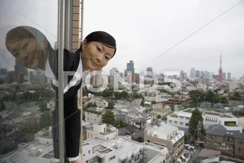 A businesswoman leaning out of a window above Tokyo cityscape Stock Photos