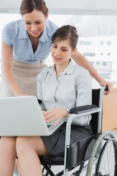 Businesswoman looking at co workers laptop who is sitting in wheelchair Stock Photos