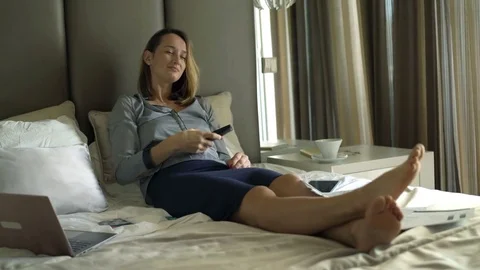 Businesswoman relaxing, watching TV and drinking coffee on bed at hotel room Stock Footage