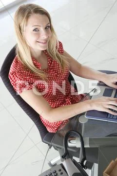 Businesswoman sitting in office typing on laptop smiling Stock Photos