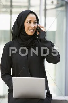 Businesswoman sitting outdoors by building with laptop using cellular phone Stock-Fotos