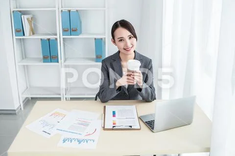 Businesswoman sitting at table in office lobby and using laptop computer. Stock Photos