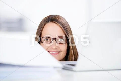 Businesswoman smiling with laptop and binder on desk Stock Photos