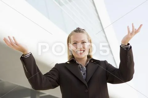 Businesswoman standing outdoors by building smiling with hands out Stock-Fotos