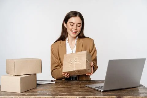 Businesswoman, store owner sitting near laptop, holding box with client order Stock Photos